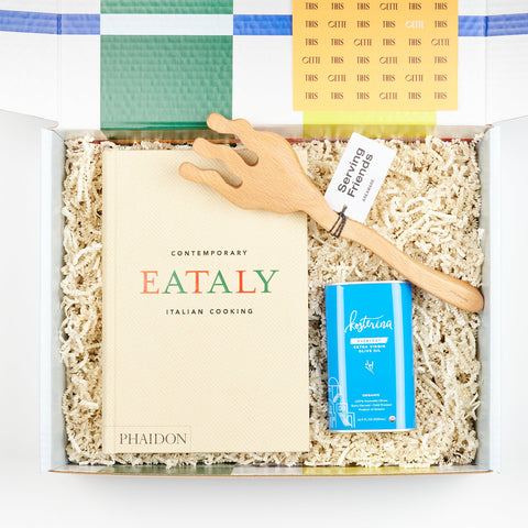an open Cette gift box showing A Cookbook set including Phaidon cookbook Eataly - Contemporary Italian Cooking, Kosterina Olive Oil, and Areaware Serving Friends wooden tongs