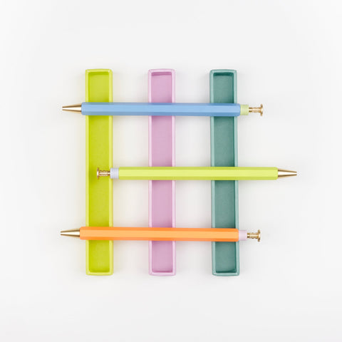 Three Papier wiggle top ball point pens in blue, yellow and orange arranged in a grid formation