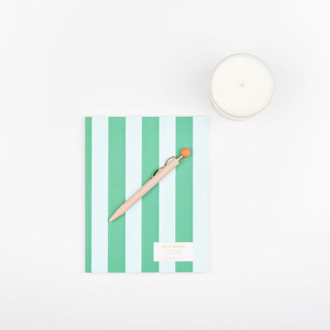 A scented Eucalyptus and Lavender Slow North frosted glass soy wax candle, a Papier Curve ballpoint pen in pink, and a perfect bound journal with a pastel striped pattern
