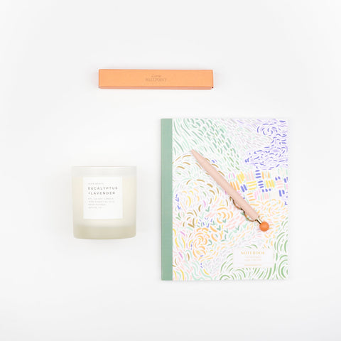 A scented Eucalyptus and Lavender Slow North frosted glass soy wax candle , a Papier Curve ballpoint pen in pink, and a perfect bound journal with a pastel brushstroke pattern