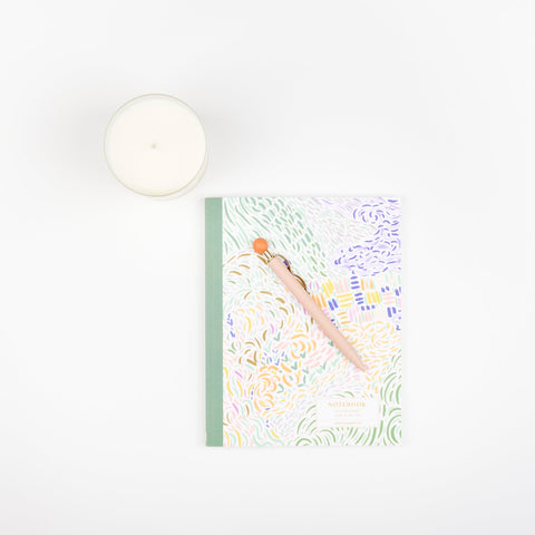 A Slow North frosted glass soy wax candle, a Papier Curve ballpoint pen in pink, and a perfect bound journal with a pastel brushstroke pattern