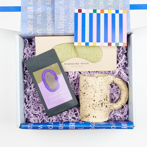 an open Cette Gift Box showing a Slow North Migraine Eye Mask, Utility Objects Eggshell Speckled Ceramic Mug, and Rosewood and Silver Lights Out loose leaf tea