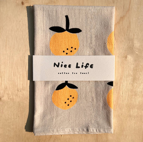 Printed cotton tea towel with featuring oranges and 'Nice Life' label on a wooden surface