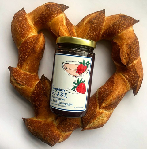 Bottle of Josephine's Feast strawberry and pink champagne jelly surrounded by a bread wreath on a white background