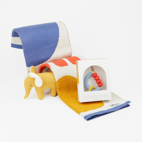 Colorful baby blanket folded in an arch with a yellow stuffed elephant and baby teether