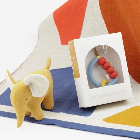 Close up of baby blanket with shapes, a yellow plush elephant and red, blue and yellow teether