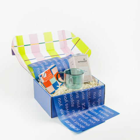 Teal glass mug with hot chocolate tin and colorful coasters in a gift box