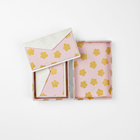 A pink card with gold flower details in it's envelope on top of it's open pink box