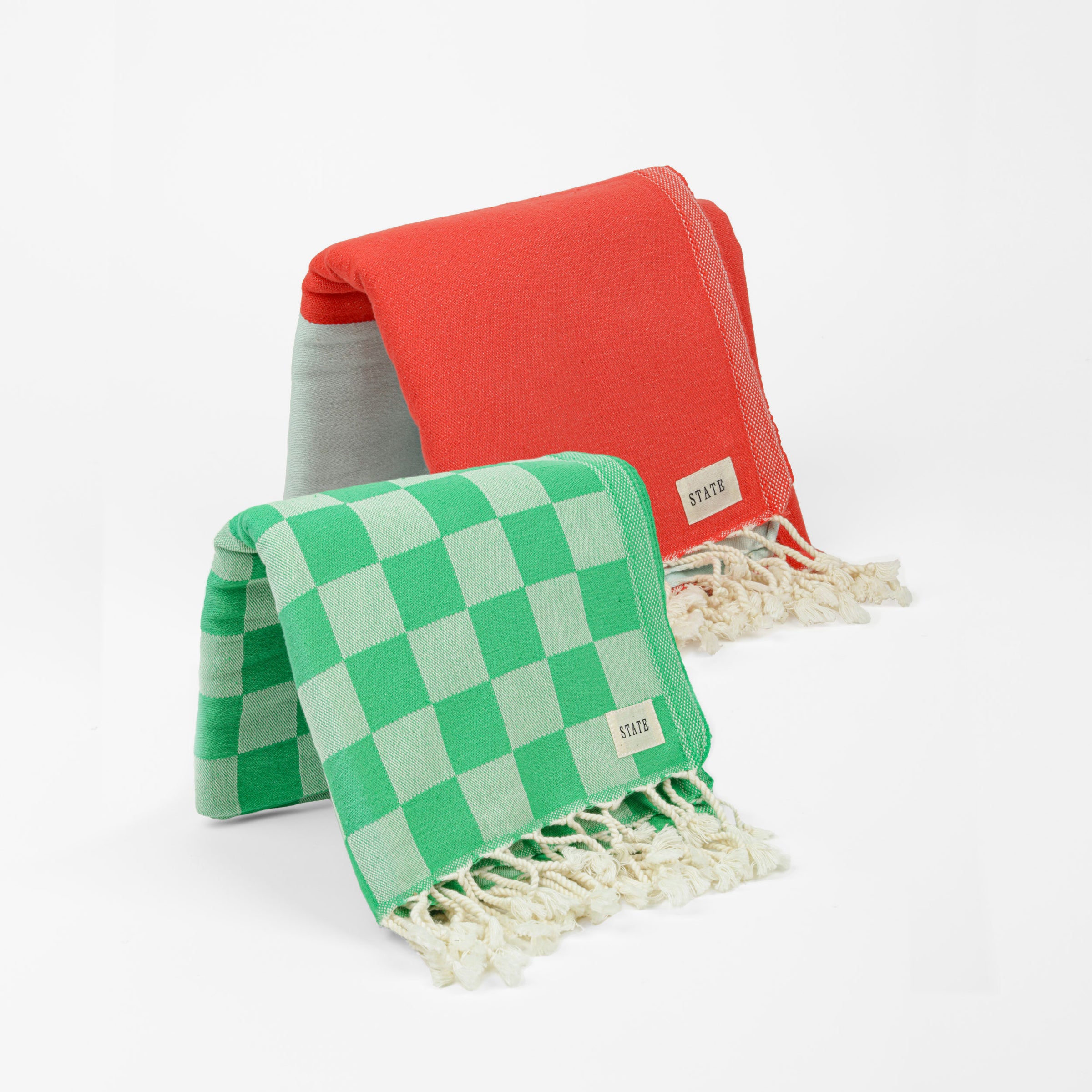 One green checkered towel with tassels and one red and blue towel with tassels