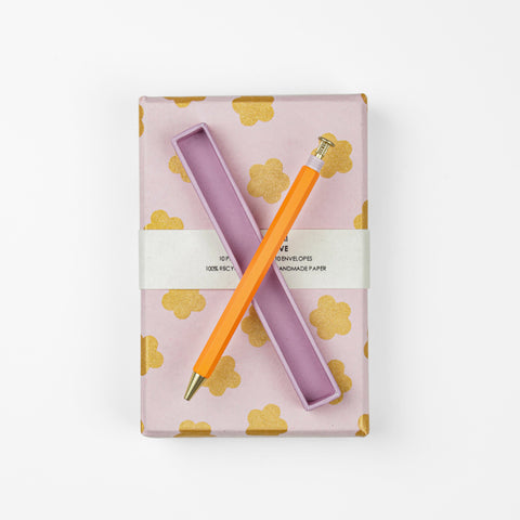 An orange pen in it's pink box on top of a pink box of cards with gold flower detail