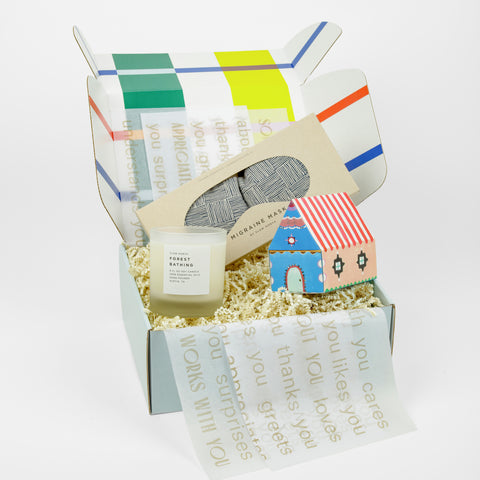 A candle, colorful box of matches in a box shaped like a house and a dark blue eye mask all in a colorful box