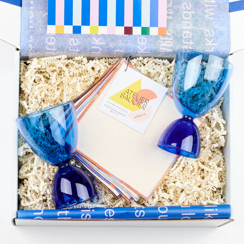 a gift box showing a set of four Atelier Saucier pale pink cloth cocktail napkins and two dark blue and light blue Mamo classic glasses