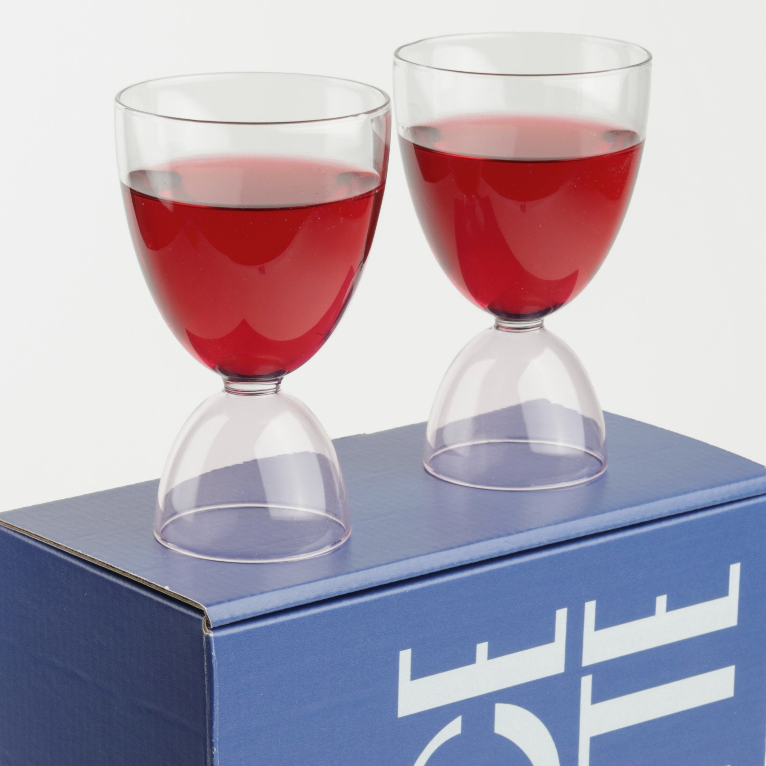 Two clear and pick glasses with red liquid in them standing on top of a blue box