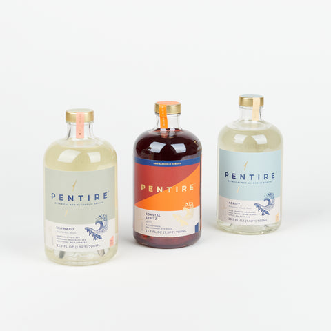 three large glass bottles of Pentire Non-alcoholic aperitif in the flavors Seaward, Coastal Spritz, and Adrift