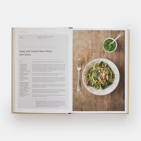 Eataly Italian Cookbook open and showing a recipe for Pasta with Pesto and clams and a photograph of the dish on a wooden table next to a fork and cup of pesto