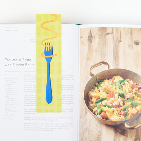 a bookmark showing pasta swirling around a fork sitting on an open cookbook showing a recipe and photograph of tagliatelle