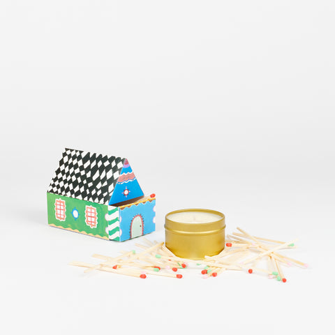 A matchbox in the shape of a house next to a small tin candle with matches surrounding the candle