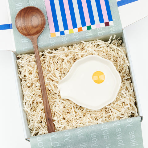 An open gift box showing Cette's Sunny Side - a gift set that included a wooden walnut spoon and a ceramic egg-like spoon rest