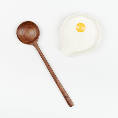 a walnut cooking spoon next to a ceramic spoon rest that resembles a fried sunny side up egg