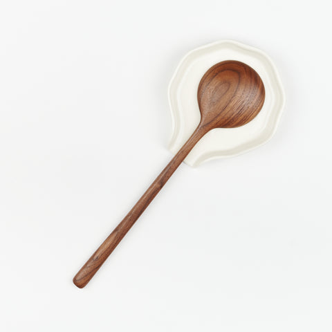 walnut spoon sitting face down on a circular white ceramic spoon rest