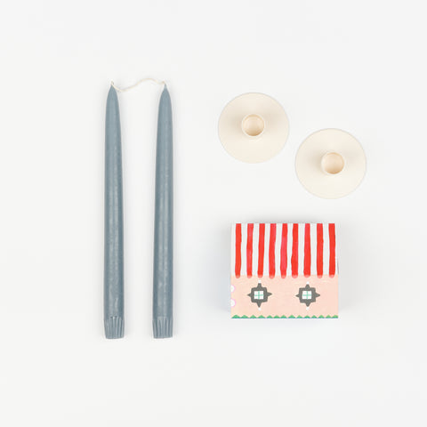 Blue gray taper candles, pair of off-white metal Hawkins New York Candle Holders, and State the Label box of matches in the shape of a house with colorful illustrations