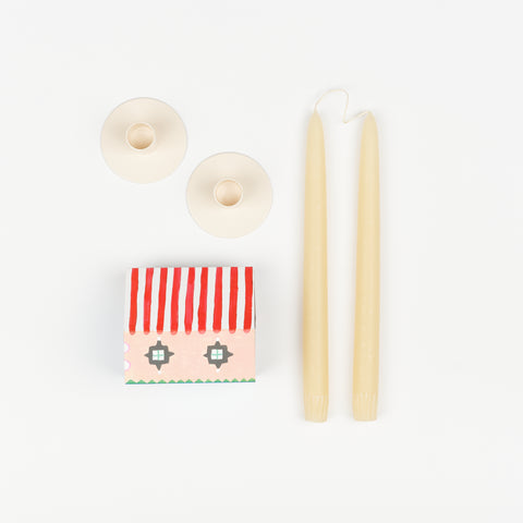 Ivory taper candles, pair of off-white metal Hawkins New York Candle Holders, and State the Label box of matches in the shape of a house with colorful illustrations