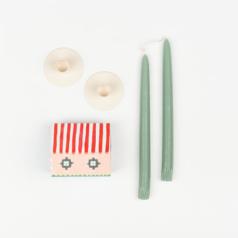 Sage green taper candles, pair of off-white metal Hawkins New York Candle Holders, and State the Label box of matches in the shape of a house with colorful illustrations