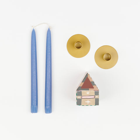 Baby blue taper candles, pair of yellow metal Hawkins New York Candle Holders, and State the Label box of matches in the shape of a house with colorful illustrations