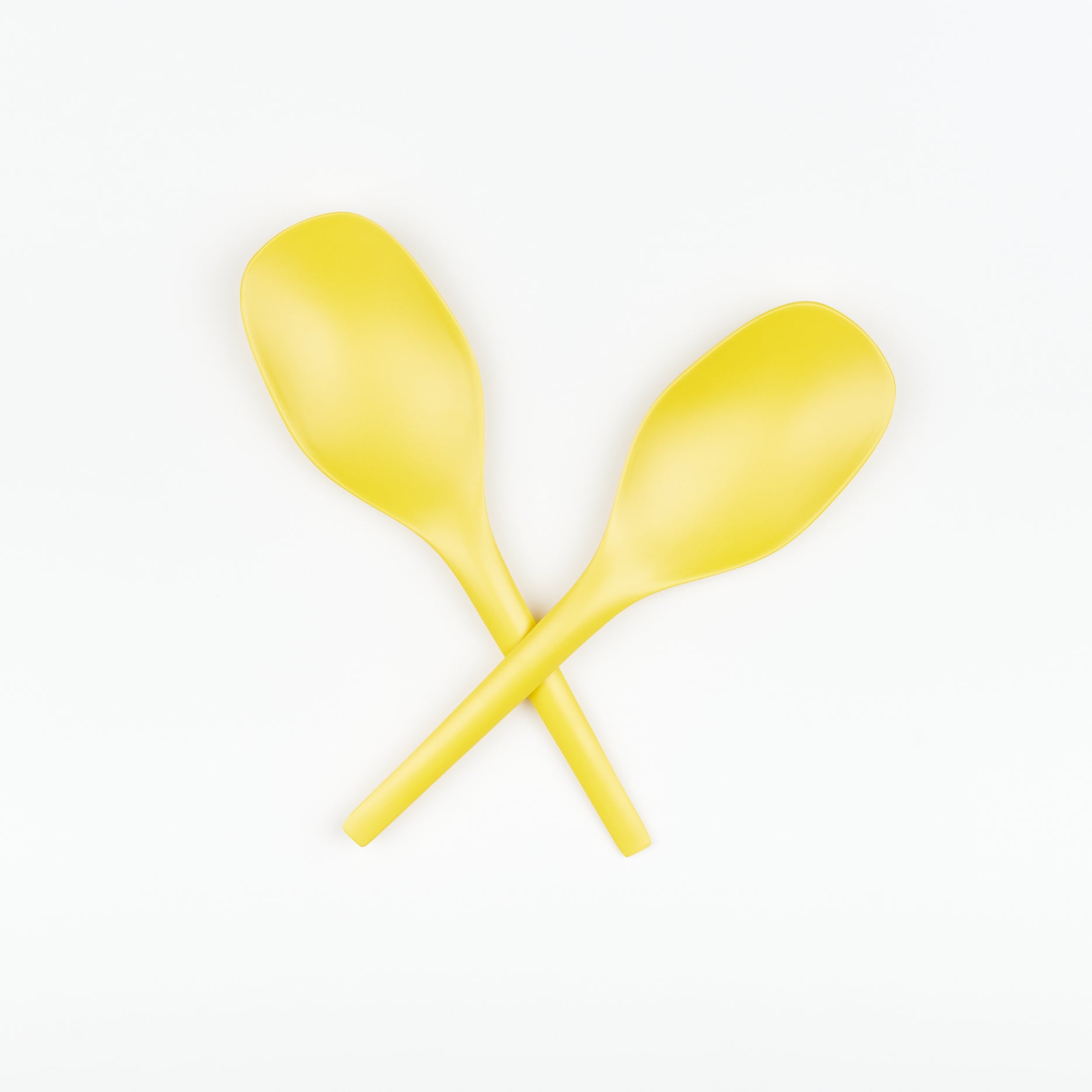 A pair of bright lemon yellow EKOBO serving spoons crossed in the shape of a X