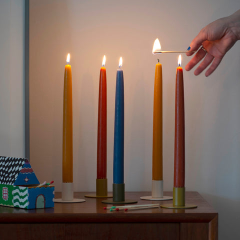 an arrangement of candle tapers on a wooden piece of furnature with a hand reaching in with a lit match to light the last candle