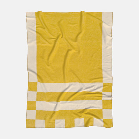 A Manifatura Merino Wool blanket with asymmetrical geometric pattern in yellow and off-white colors