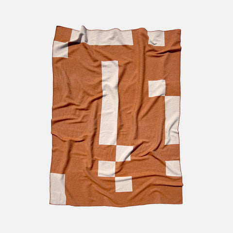 A Manifatura Merino Wool blanket with asymmetrical geometric pattern in burnt orange and pink colors
