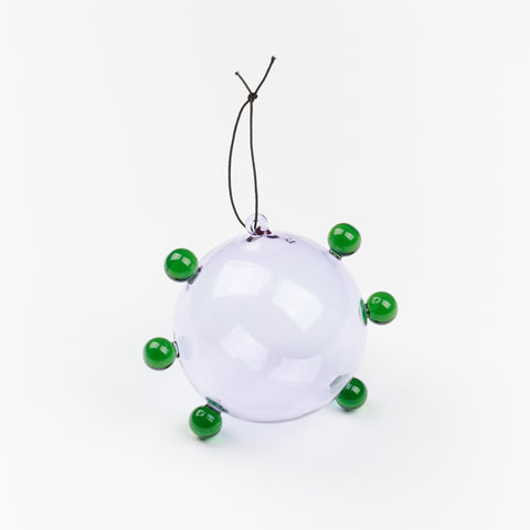 A Sophie Lou Jacobsen glass ornament that is lilac with green glass spheres and a small black string to hang it with