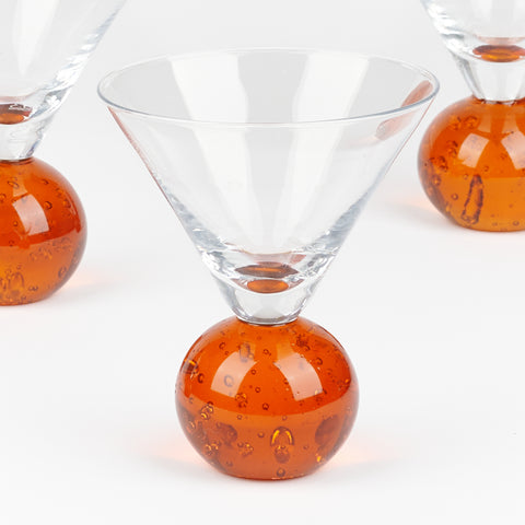 close up of a martini glass with orange rounded circular glass base with bubbles inside