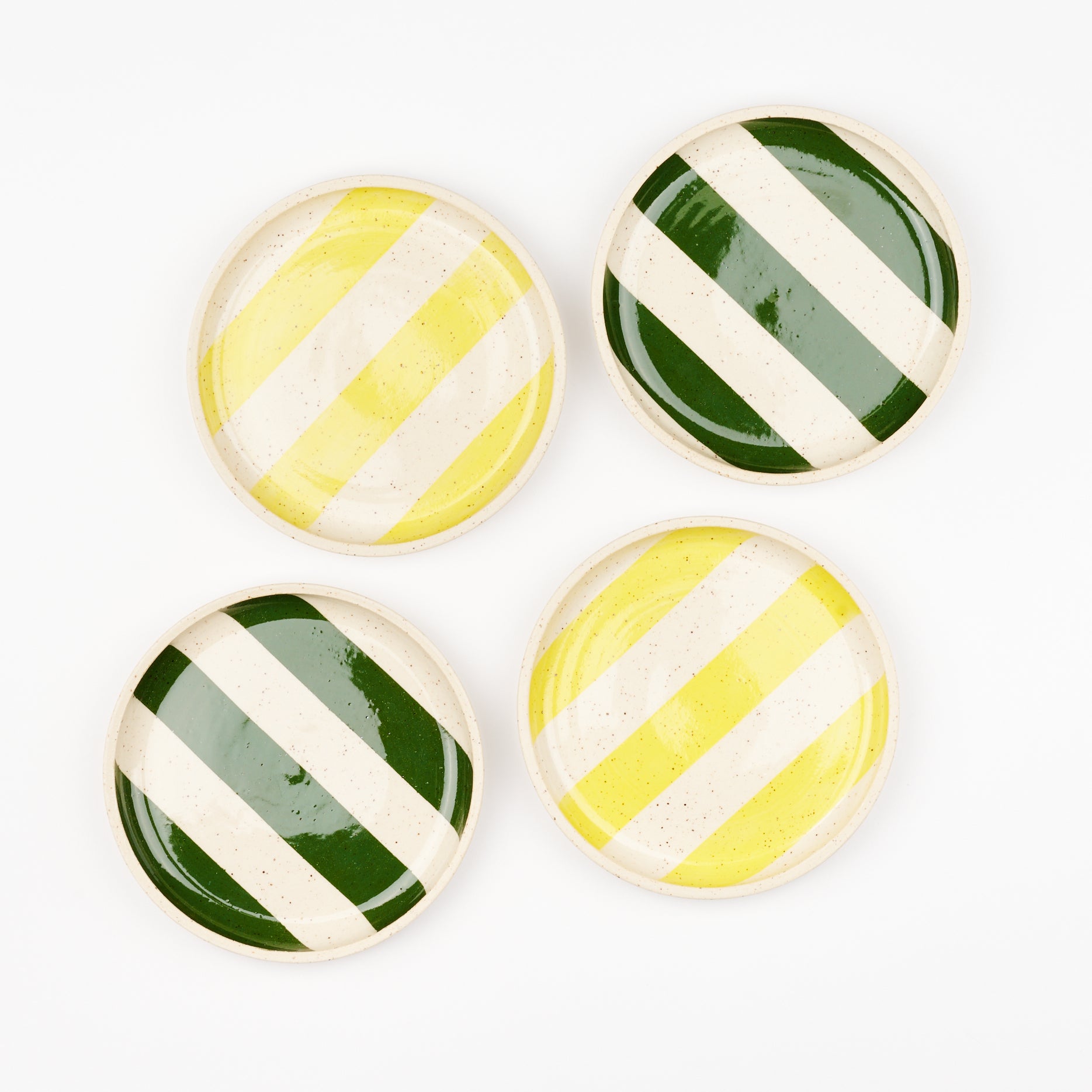 Four striped ceramic plates made by Libby Hruska - two have dark green stripes and two have lemon yellow stripes