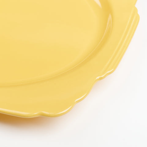 A close up of a yellow vintage ceramic serving plate with curved decorative edges