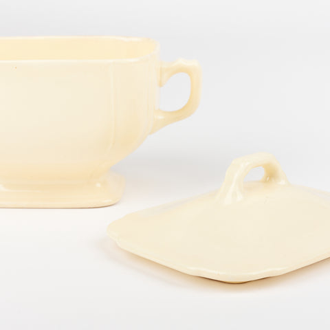 a close up view of a white ceramic sugar bowl with its matching lid sitting beside it at an angle
