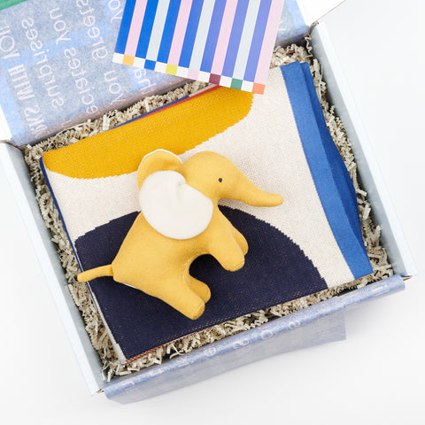 open gift box with folded baby blanket and a small yellow soft toy elephant