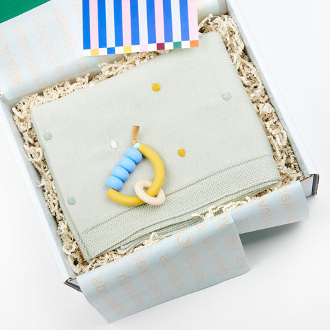 open baby gift box with pale blue tissue paper and featuring a mint green baby blanket and matching teething ring