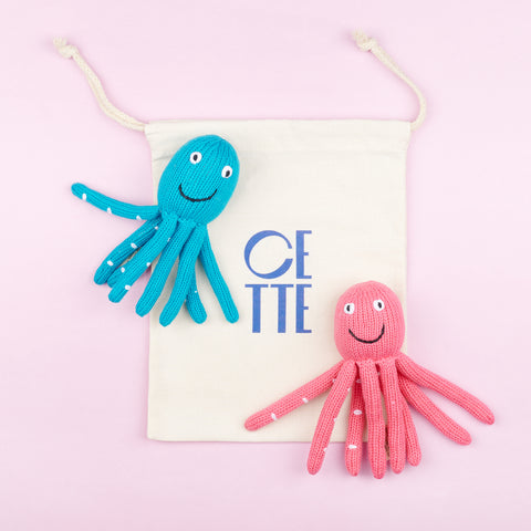 two plush knit octopus baby rattles one blue and one pink laying on a Cette custom drawstring bag
