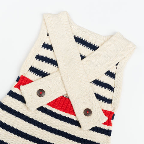 back side of a cream knit baby romper showing crossed straps that close with wooden buttons