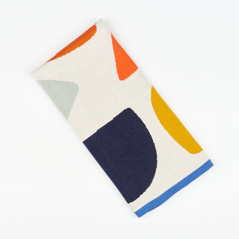 A folded kids blanket by Sophie home featuring multi-colored shapes on a cream base with blue trim