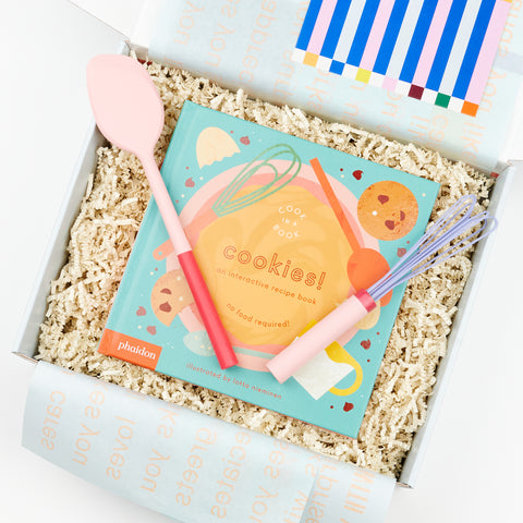 An open gift box with Phaidon Kids Cook in a Book - Cookies!: An Interactive Recipe Book and a pink mini spatula and a pink and purple mini air whisk