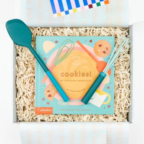 An open gift box with Phaidon Kids Cook in a Book - Cookies!: An Interactive Recipe Book and a green and blue mini spatula and a green mini air whisk