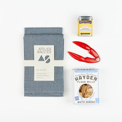 an artful arrangement of the a hickory stripe tea towel set, a tin of seafood seasoning, a red lobster cracker and a box of mini crackers