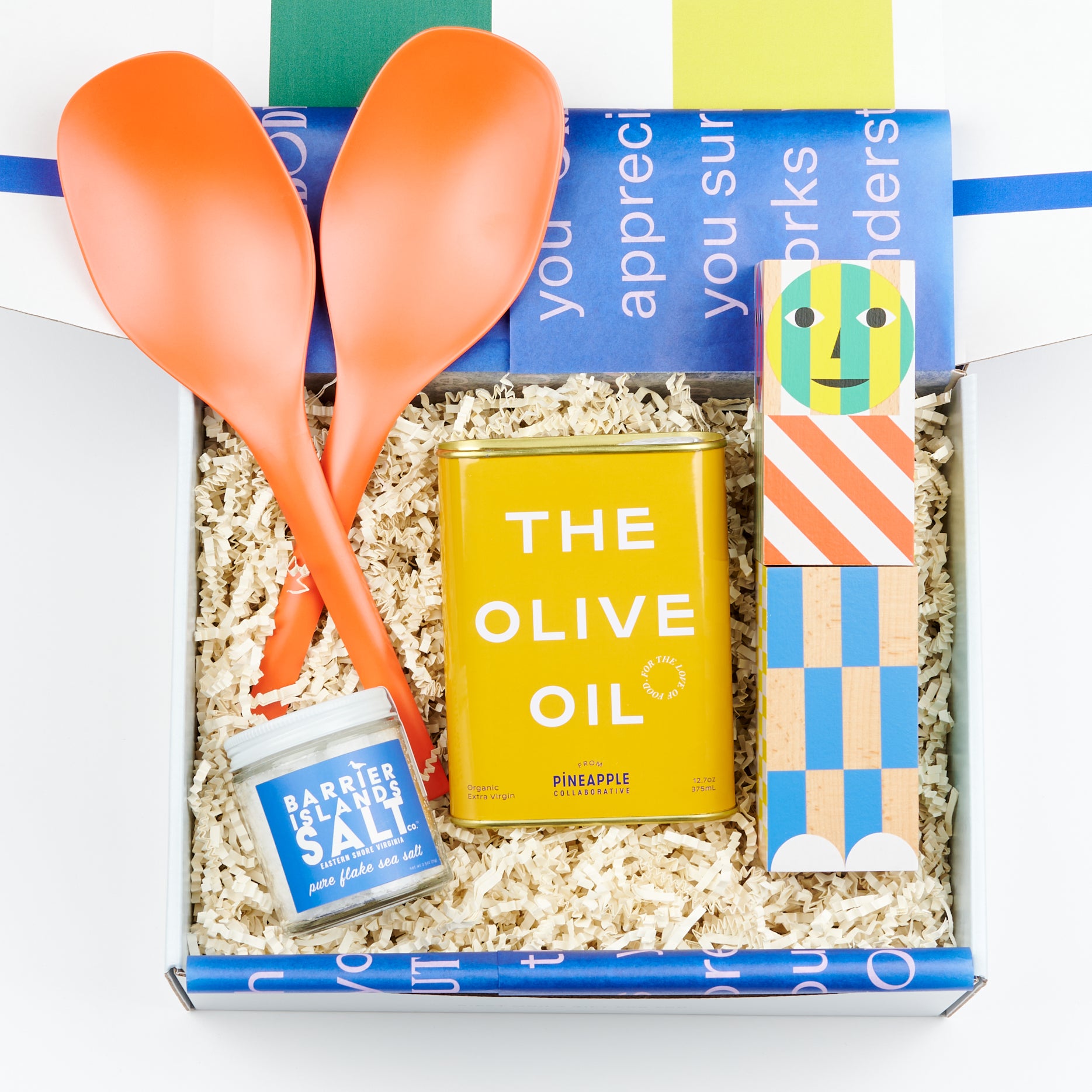 a CETTE gift box showcasing a pair of bright orange EKOBO serving spoons, A salt or pepper grinder, a tin of olive oil and a jar of flake sea salt