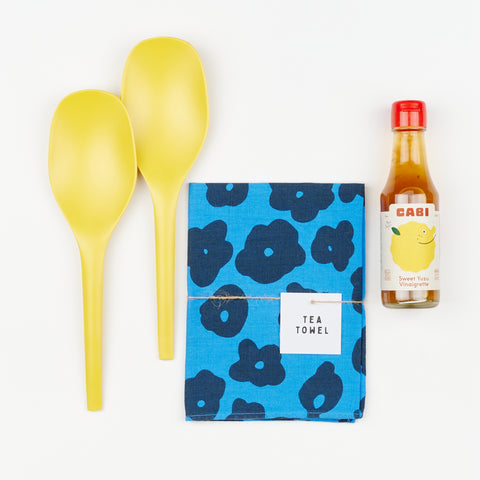 Two yellow salad tongs, a blue tea towel with floral pattern and a bottle of vinaigrette