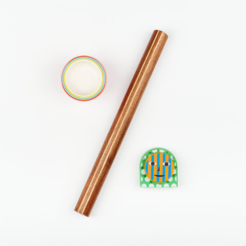  A handmade rolling pin, four colorful bamboo Ekobo measuring cups nested into one, and an Areaware Kitchen Timer arranged artfully on a white backdrop