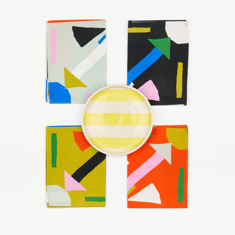 Four colorful geometric napkins with a ceramic plate with yellow stripes