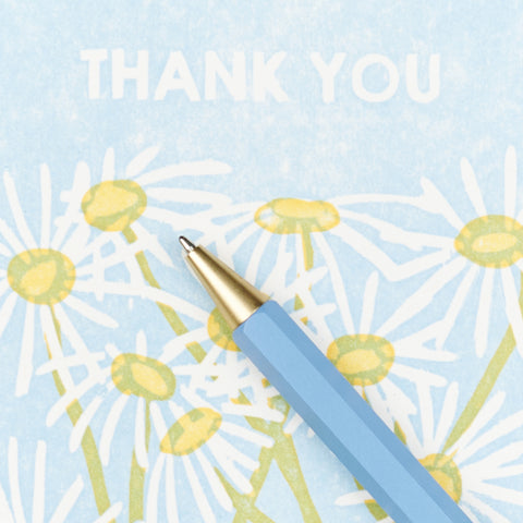 a close up view of a blue pen on thank you card with a daisy illustration